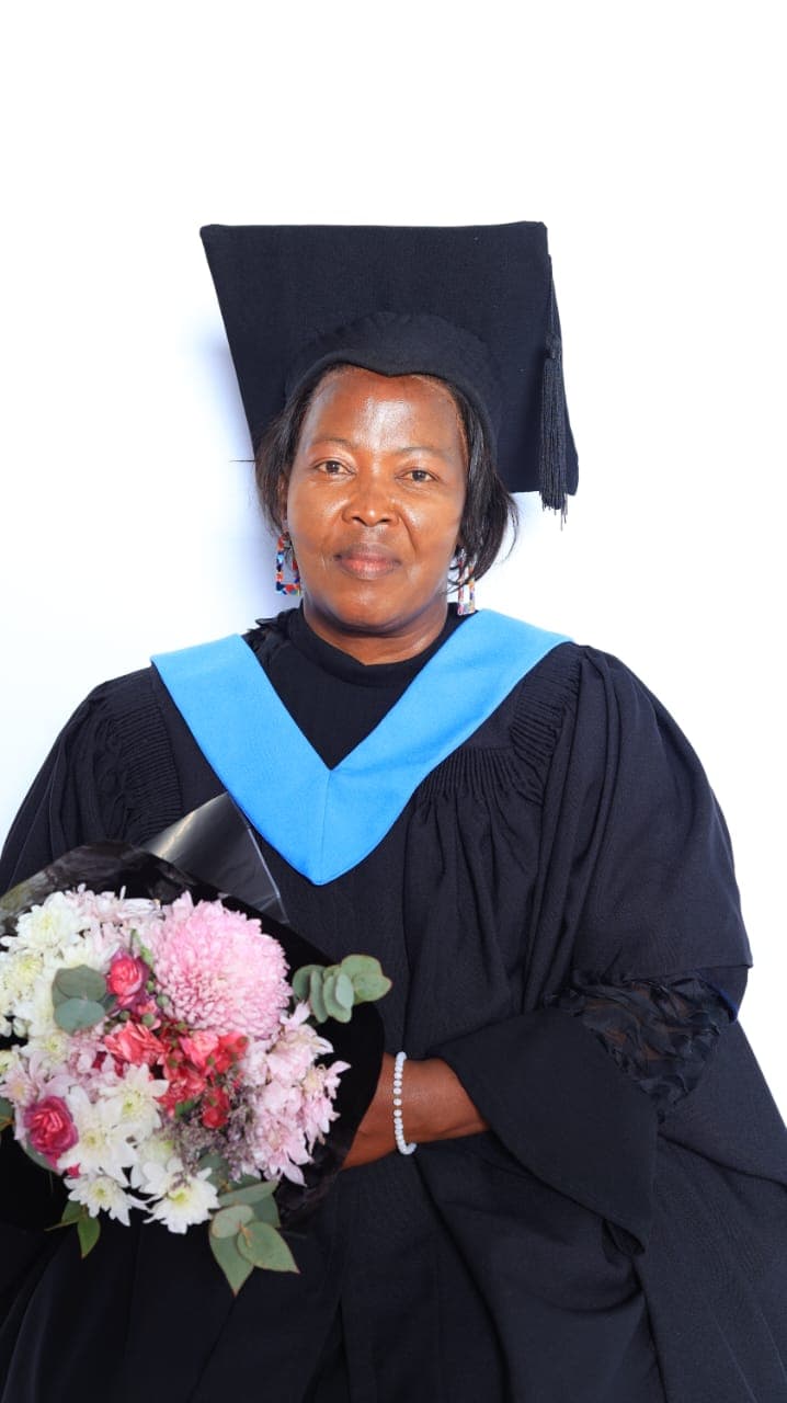 A GE College graduate in academic dress holding a bouquet